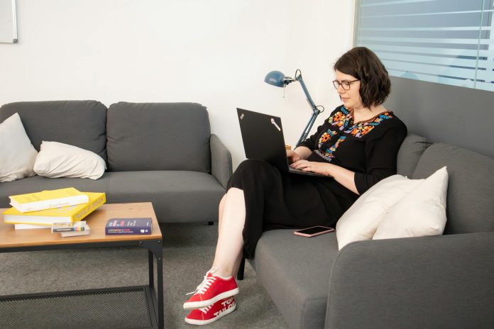 A person working on their laptop while seated on a sofa in a coworking office