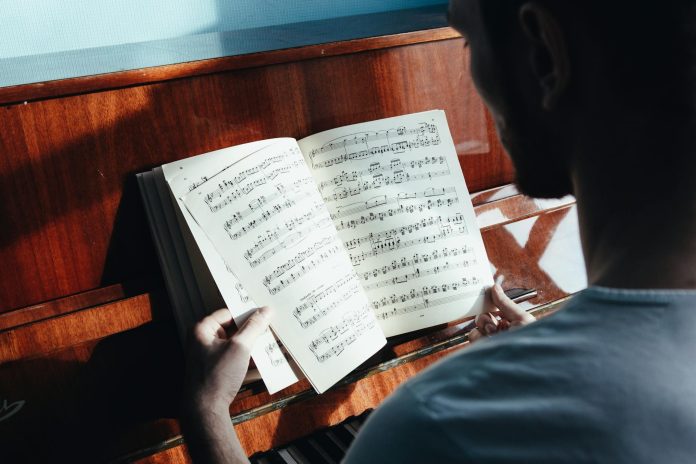 Back view of crop anonymous male pianist watching music paper with written notes near piano