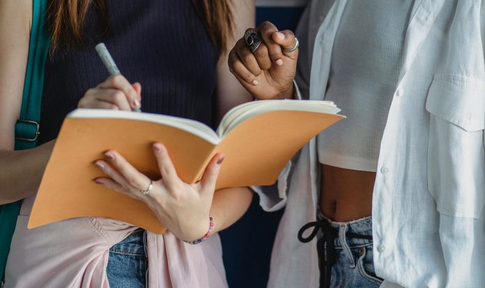 Crop diverse girlfriends writing in exercise book